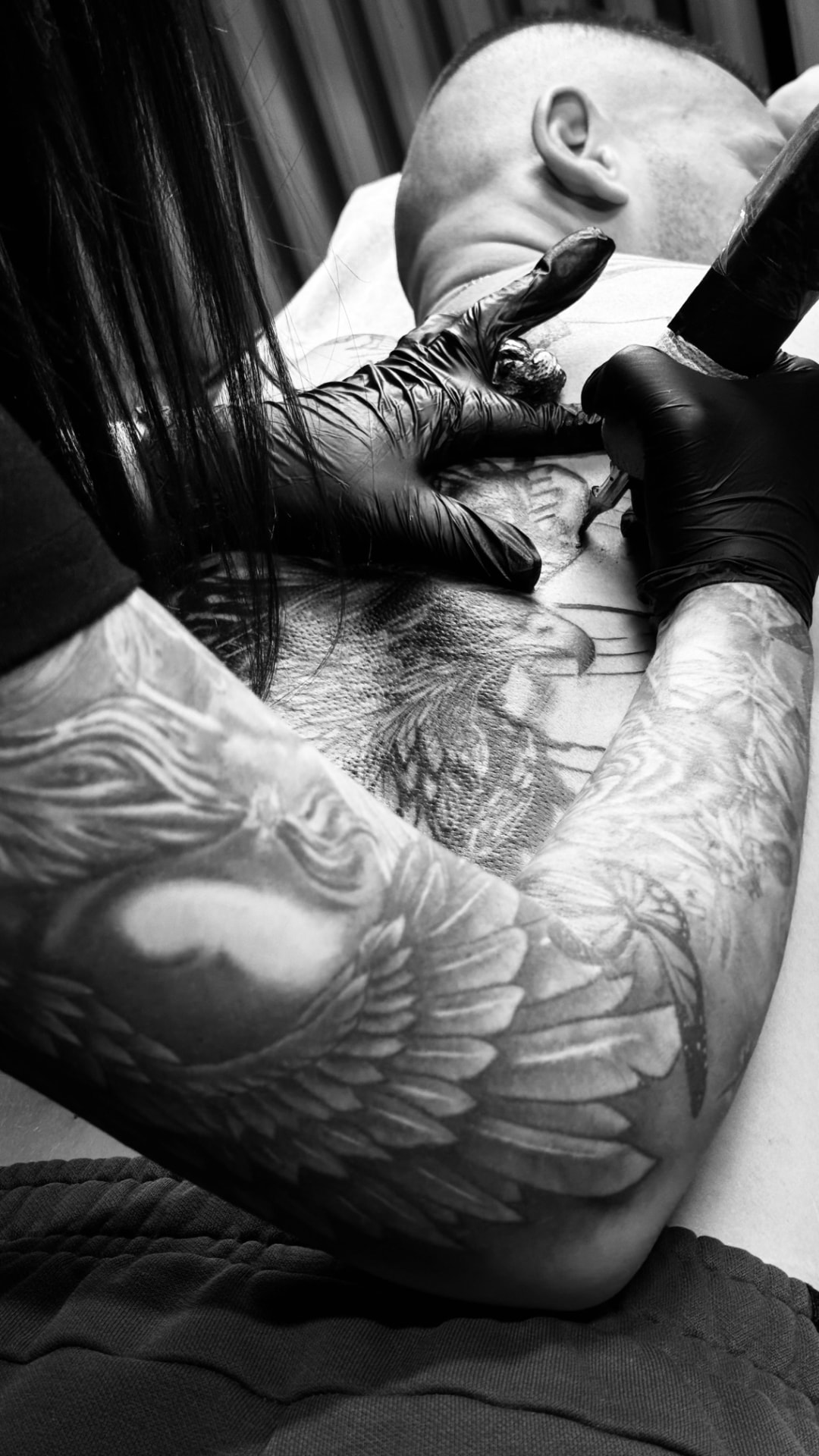 Tatoueuse gantée en train de tatouer le torse d'un client, photographie noir et blanc