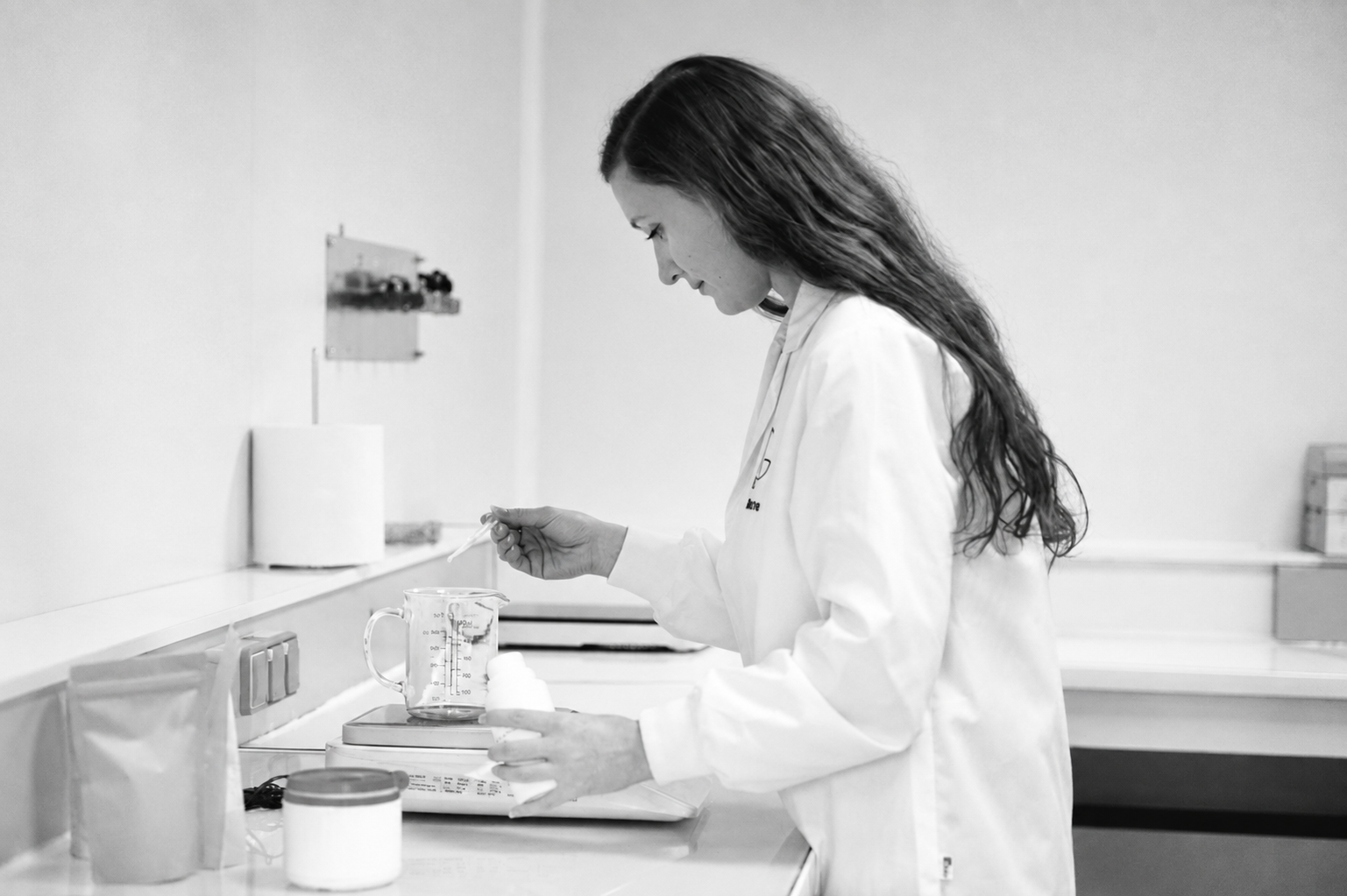 Formulatrice en blouse blanche pesant des ingrédients cosmétiques dans un laboratoire